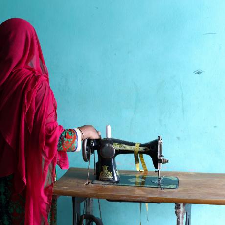 Rahima, a garment factory worker in Bangladesh, next to a sewing machine and with her back to camera