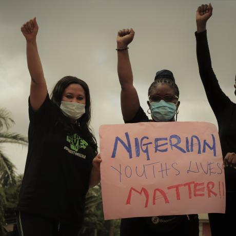 Three young women wearing masks hold sign saying 'Nigerian youth lives matter'